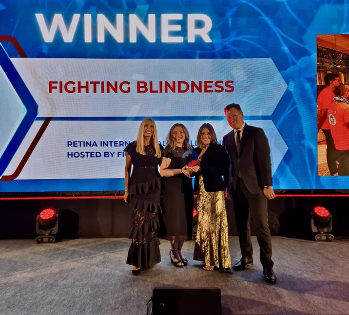 Fighting Blindness Research Officer Shannon Lee and Science Communications Officer Konstantina Karagkiozeli accepted the award on the night. Image of them on stage receiving the award together with the presenters of the awards.