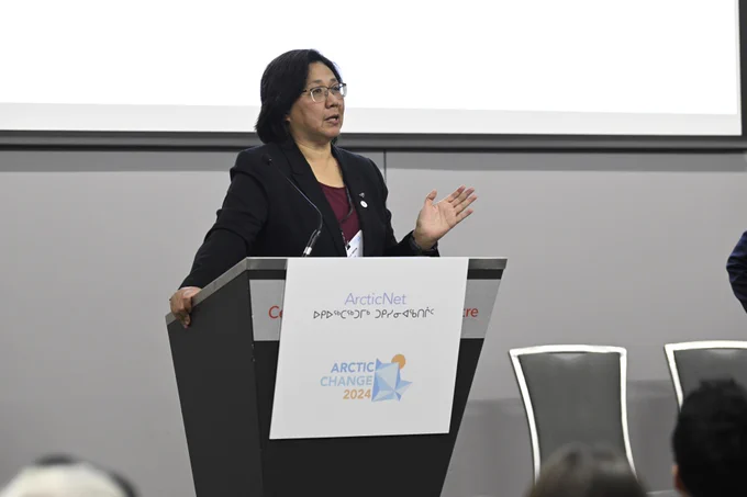 A person speaks at a podium at a conference. The podium sign reads “Arctic Net: Arctic Change 2024.”