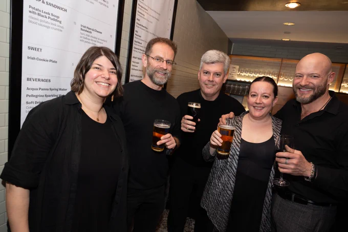 Musicians from Alarm Will Sound stand together and a raise a glass in a cafe / bar setting.