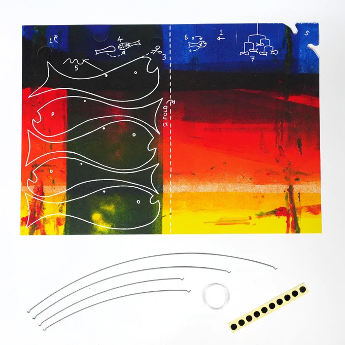 A Fish Mobile kit product shot, which consists of: a colourful printed sheet of card with instructions and cutting guides, four wires, thread, and a strip of small round stickers. 