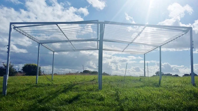 A rain shelter fills the photo. The sun shines down through the shelter, and there are few clouds in the sky.