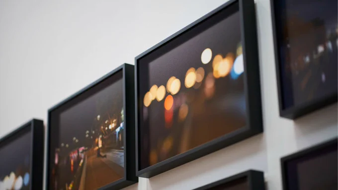 A row of photos hung on a white wall in black frames, featuring cities as night with large circles of out of focus light.