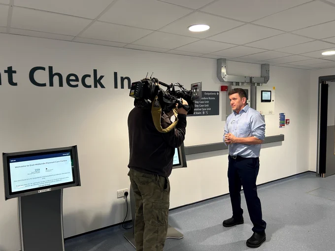 A camera man can be seen filming BBC East Midlands Today's Health Reporter Rob Sissons. Rob and the camera man are standing in the entrance area of the new East Midlands Planned Care Centre.