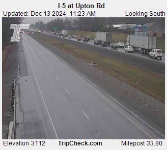 Tripcheck traffic camera view of Interstate 5 at Upton Road, milepost 33.8, looking south with a line of traffic stopped on the highway on an overcast day.