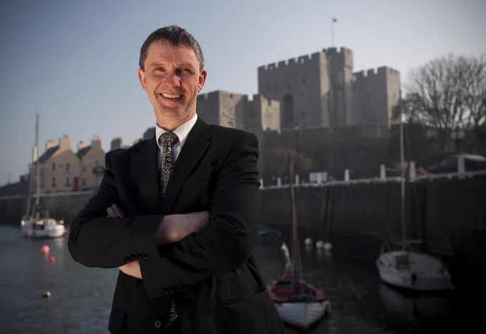 A photo of Chris Gledhill posing for a photo with his arms crossed in front of Castle Rushen in the background