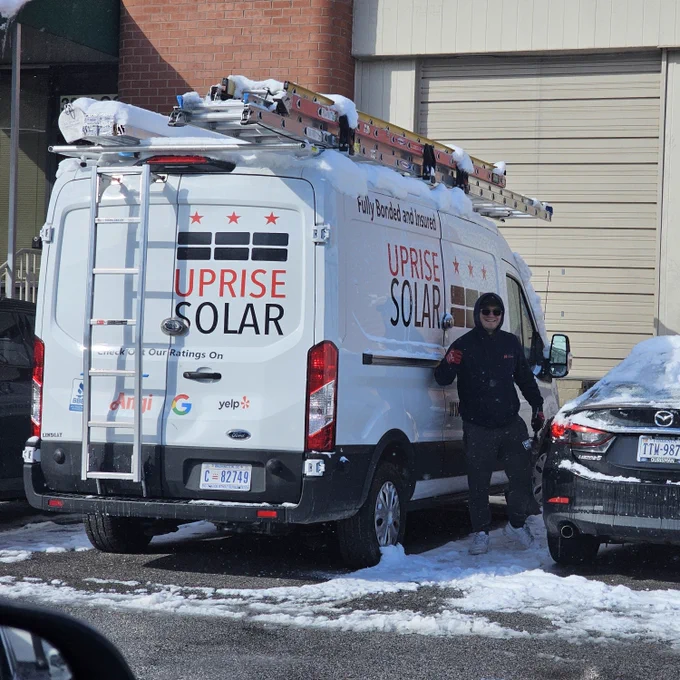 A solar installer smiles next to an Uprise Solar truck on a snowy day.