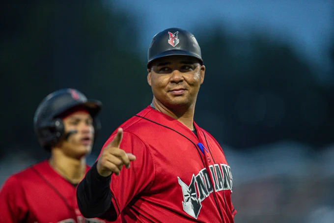 Former Indianapolis Indians manager Miguel Perez stands in the third-base coaches box and points as catcher Endy Rodríguez runs behind him.
