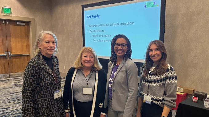 Four WestEd staff standing in front of a presentation screen displaying "Get Ready" and game instructions at the Learning Forward conference.