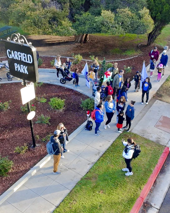Group of people walking on a path at Garfield Park, with some carrying flags.