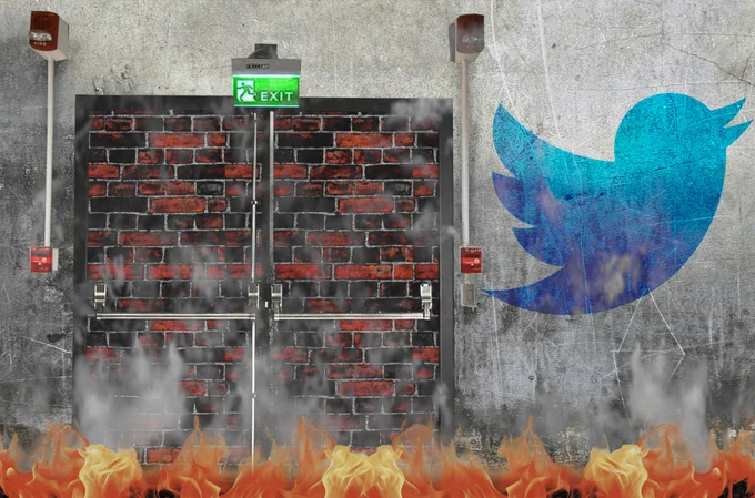 A dirty, cracked wall with a bricked-up fire-exit set into it - a pair of double-doors with crashbars, fire alarms, and a fire exit sign. To the left of the doors is a faded, dirty Twitter logo. The bottom of the frame is filled with flames, and smoke rises off of them.