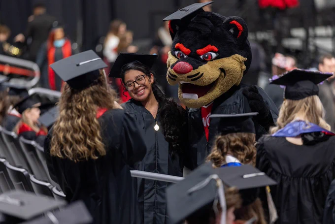 Graduate smiling at the camera during a graduation ceremony, standing near the University of Cincinnati mascot.