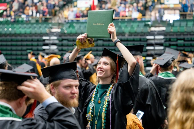 A C S U student holds their diploma up to the crowd during commencement.
