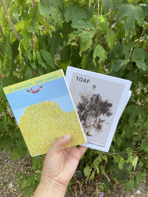 Hand holding My Lesbian Novel & TOAF in front of some leaves