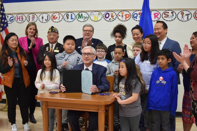Gov. Evers holds up signed bill surrounded by kids and local leaders 