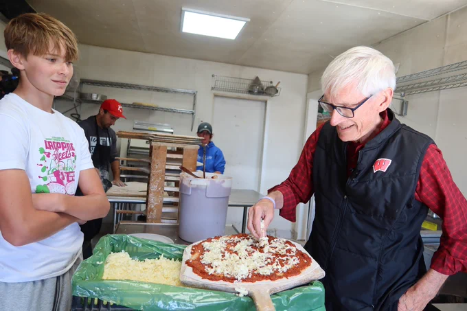 Gov. Evers sprinkles cheese on a pizza in the kitchen 