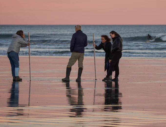 People working on a beach with the ocean and waves in the background