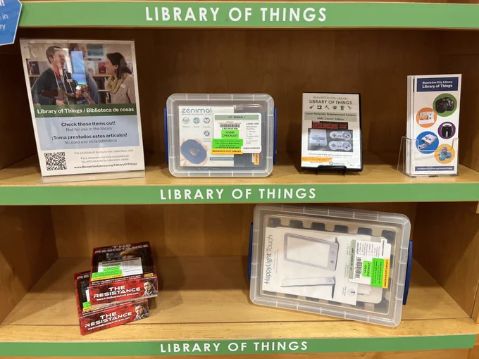 Items of two shelves that are labeled Library of Things. Zenimal, Happy Light Touch and a card game called The Resistance.