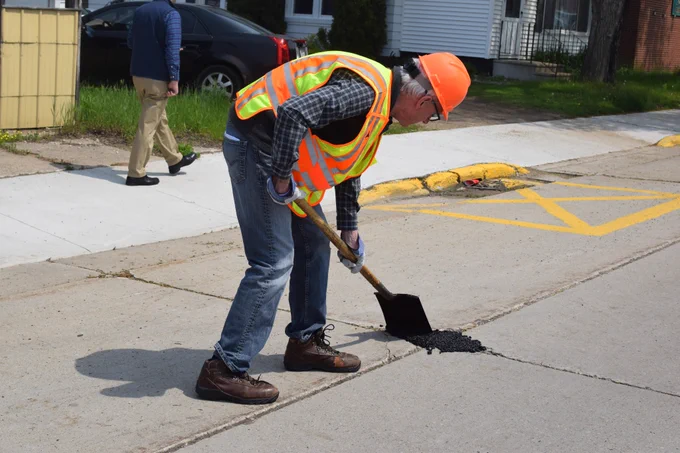 Gov. Evers fills pothole with asphalt. 