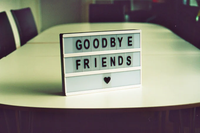 A sign standing on a table in a conference room. The sign reads "Goodbye Friends" in capital letter and with a heart on the last row of the sign. Photo by Jan Tinneberg on Unsplash