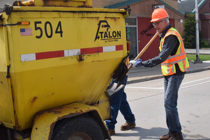 Gov. Evers shovels asphalt out of the back of a truck. 