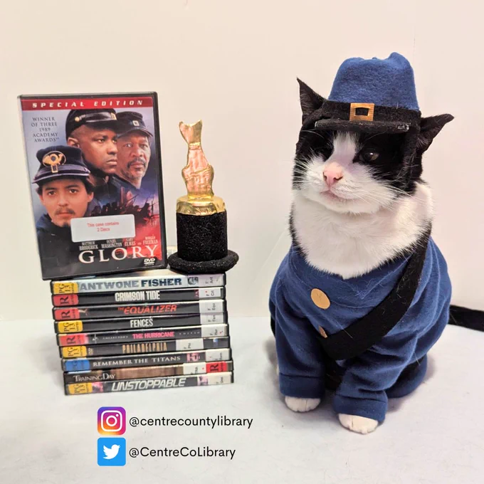 A photo of Jojo the Pirate Cat dressed in a blue Union soldier's uniform with a blue cap sitting next to a stack of DVDS and the film "Glory" to emulate Private Silas Trip from the film. A mini cat Oscar statue sits next to the "Glory" DVD.
