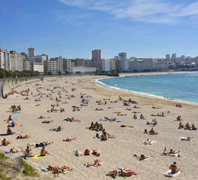 Playa con forma de letra "C" en la ciudad. Día soleado con gente tumbada tomando el sol.