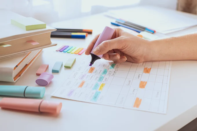 A student designing a weekly training schedule on a white table with colorful markers and stickers.
