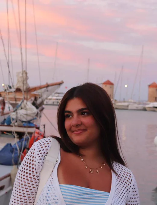 Natassa stood in front of a harbour, with a sunset behind her
