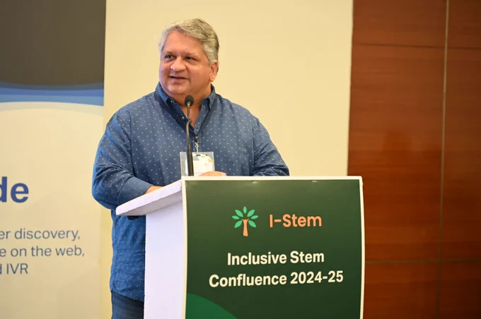 A middle-aged man with gray hair speaking at a podium displaying the "I-Stem, Inclusive Stem Confluence 2024-25" logo.