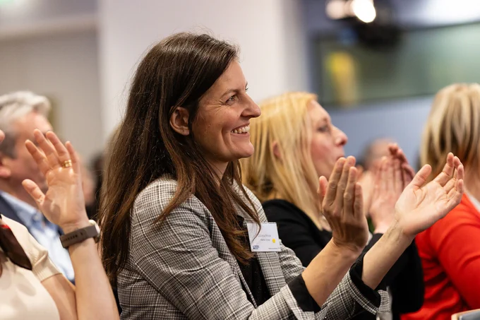 Audience member smiling and clapping at an event.