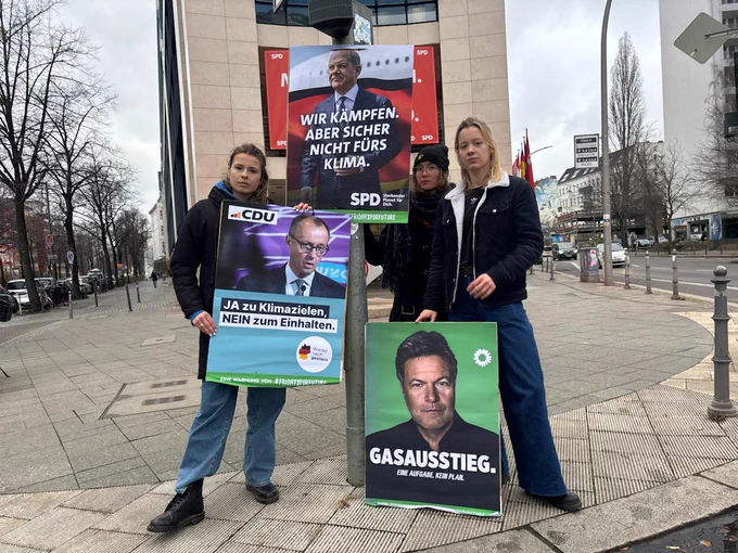 Drei junge Aktivistinnen stehen auf einem Gehweg und halten Protestplakate vor Parteizentralen. Die Plakate kritisieren Klimapolitik: ‚Ja zu Klimazielen, Nein zum Einhalten‘ (CDU), ‚Gas-Ausstieg. Eine Aufgabe, kein Plan‘ (Grüne) und ‚Wir kämpfen, aber sicher nicht fürs Klima‘ (SPD). #FridaysforFuture