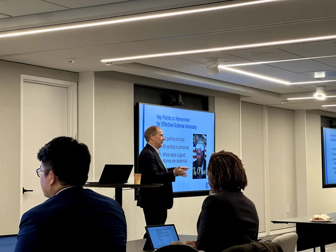 A man presents a powerpoint on science-policy to a group of people. 
