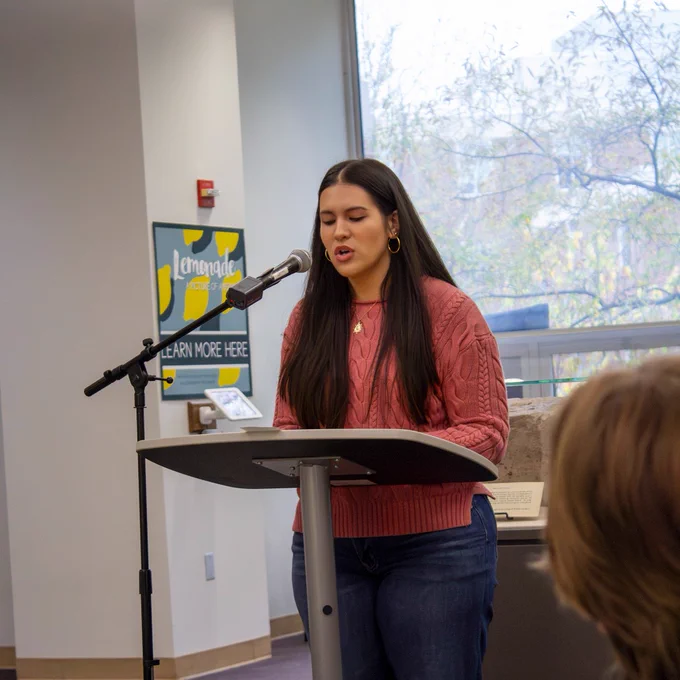 Student reads her short story to a group of listeners in the lobby of Swem library.