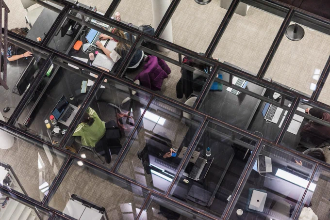 Students working on laptops seen from above through glass panels.