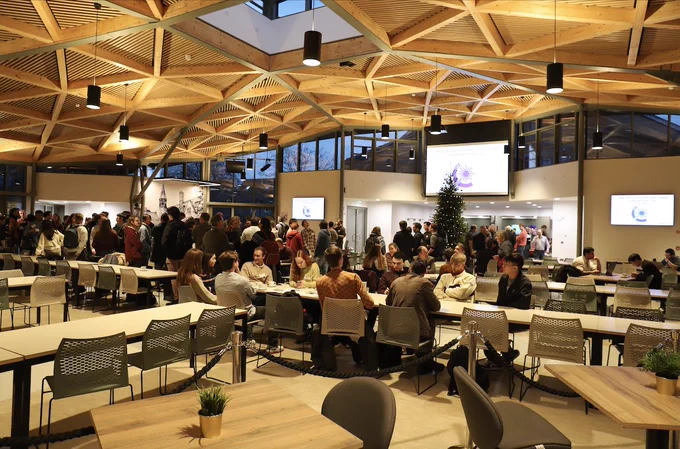hall with modern ornate ceiling and rows of tables. many people are milling around, chatting.