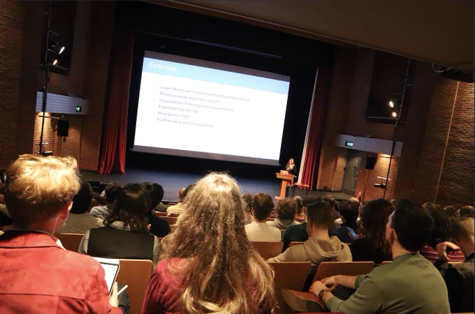 delegate gives a talk in the lecture theatre. The lecture theatre is dark and ornate with low, warm lighting and large red curtains.