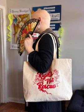 A person holding a white canvas bag that reads "Rights Not Rescue"