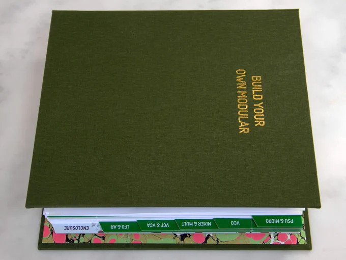 Image of Build Your Own Modular book in binding, with green cover and tabs (that form PCBs) plus marbled interior in green and pink splotches.
