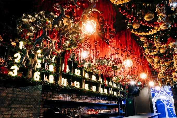 A bar decorated for Christmas. It includes a countdown from 1 through 25 and a canopy of Christmas ornaments and garland.