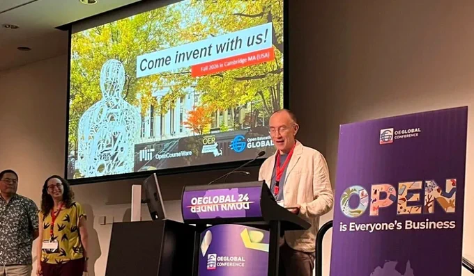 OpenCourseWare director, Curt Newton, presenting at the OEGlobal Conference podium with a slide titled "Come invent with us!" displayed in the background, and a banner reading "OPEN is Everyone's Business" beside the podium. Attendees are visible in the foreground.