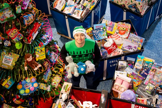 jason poses in the middle of toys while holding 3 stuffed animals