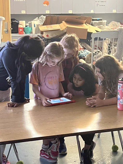 A group of girls gathered around a tablet to share their coding