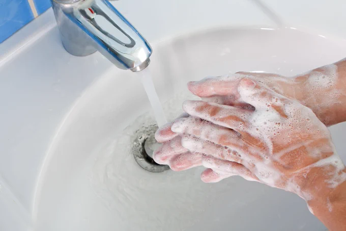 Image of hands covered in soap and being washed under a bathroom tap.