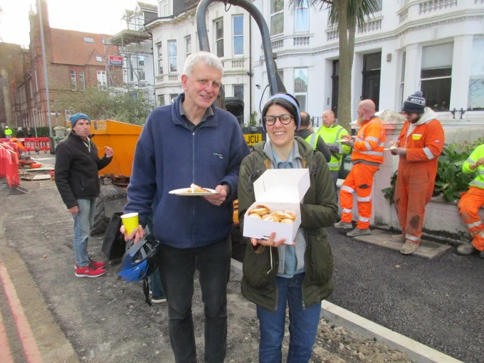 Cllr Trevor Muten (left) and Iliana from Bricycles (right) with mince pies. Max in background (left) and contractor staff in hi vis (right) on half-built  active travel facility, part of the A23 Active Travel scheme Phase 1.