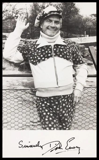 A black-and-white photography of the English comedian Dick Emery looking especially jovial as he waves at the camera in a matching floral tracksuit and flat cap. 

Credit: Dick Emery waving in a park. Photograph, 197-. Source: Wellcome Collection.
