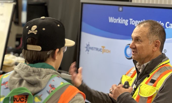 Two individuals in safety vests engaging in a conversation with a third person in front of a 'Spectra Tech' presentation screen.