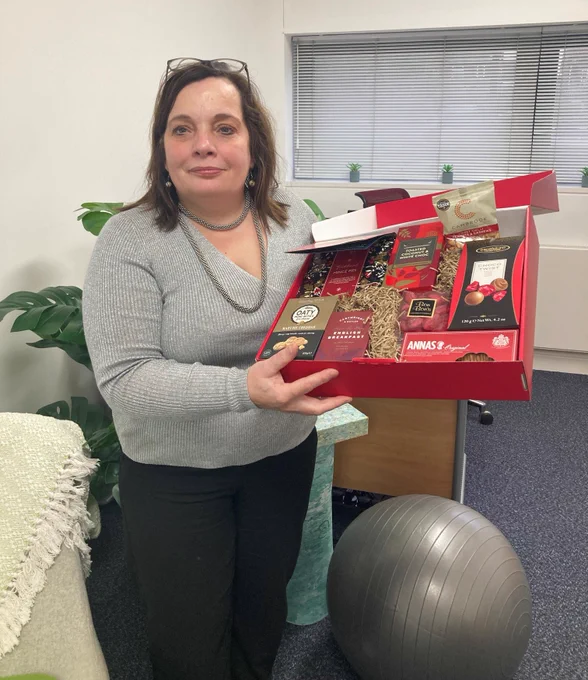 Photo of Paula stood smiling and holding the luxury Christmas hamper.
