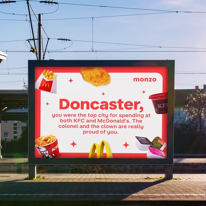 A billboard at a train station reading: 'Doncaster, you were the top city for spending at both KFC and McDonald’s. The colonel and the clown are really proud of you.' Surrounded by images of fried chicken, chips and dipping sauces.