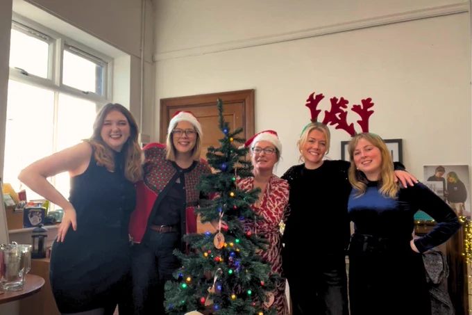 The core staff team at Stellar Quines smile at the camera with a Christmas tree.