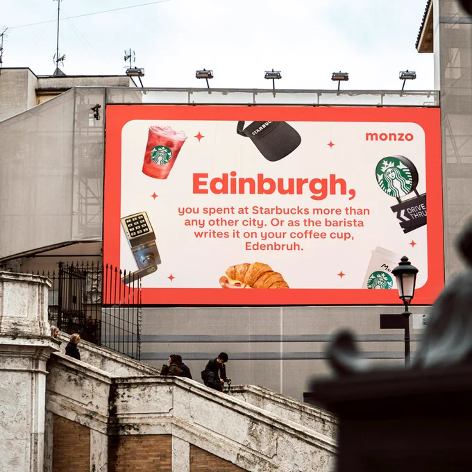 A billboard on the side of a building reading: 'Edinburgh, you spent at Starbucks more than any other city. Or as the barista writes it on your coffee cup, Edenbruh.'. Surrounded by iced drinks and a croissant.
